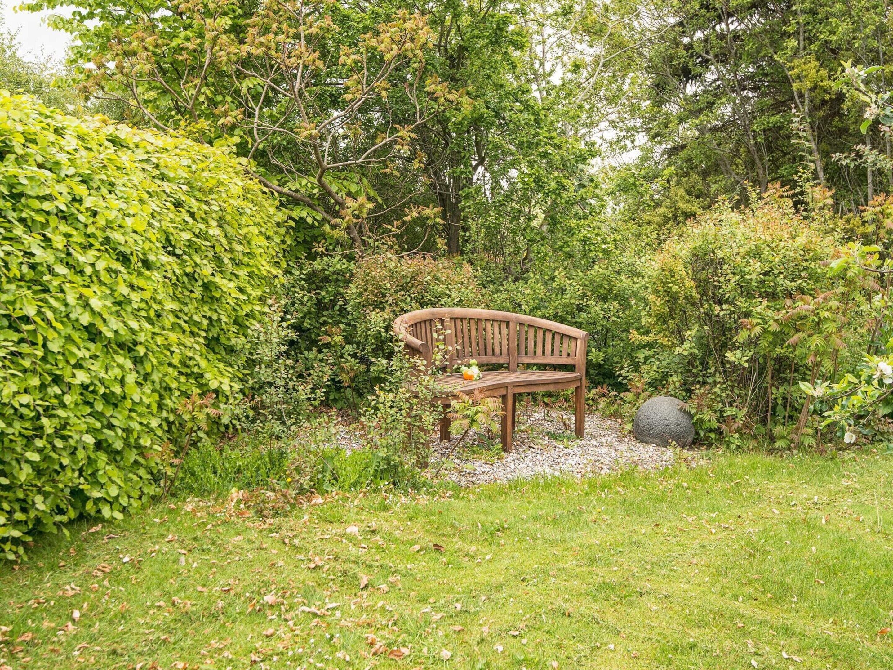 Eine Bank in einem Garten mit dichtem Grün und einem großen Felsen.