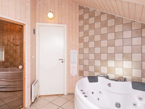 A bathroom with a wooden wall, a white door, a tiled wall, and a white bathtub with multiple jets. - Luxury Retreat With Spa - By Traum Ferienwohnungen (Sydlangeland)