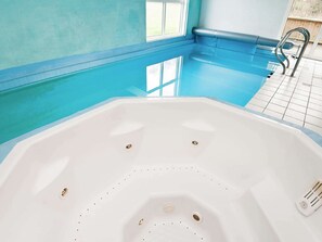 A large indoor swimming pool with a white hot tub in the center.