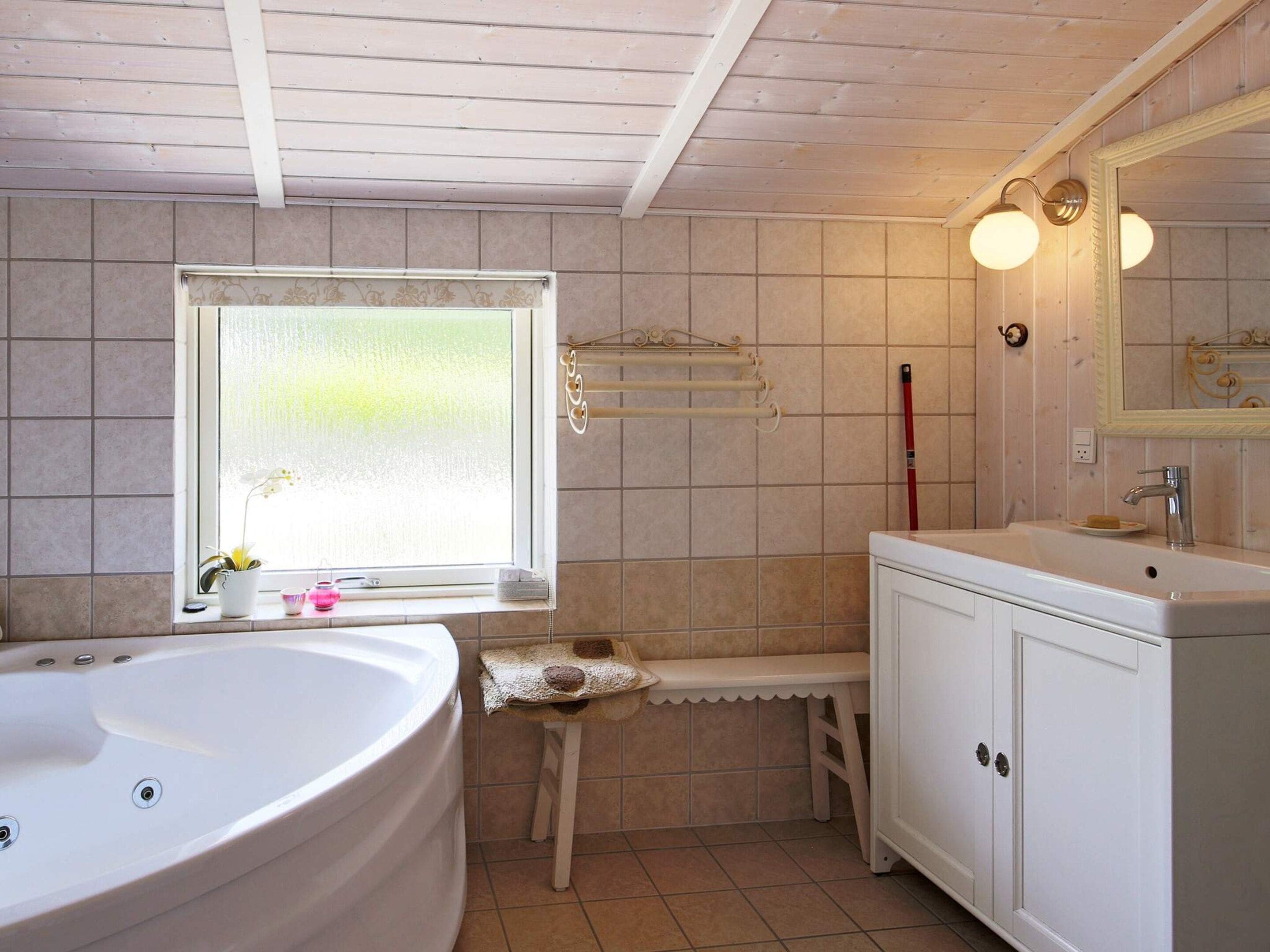 A bathroom with a large bathtub, a window with frosted glass, a towel rack, and a vanity with a mirror.