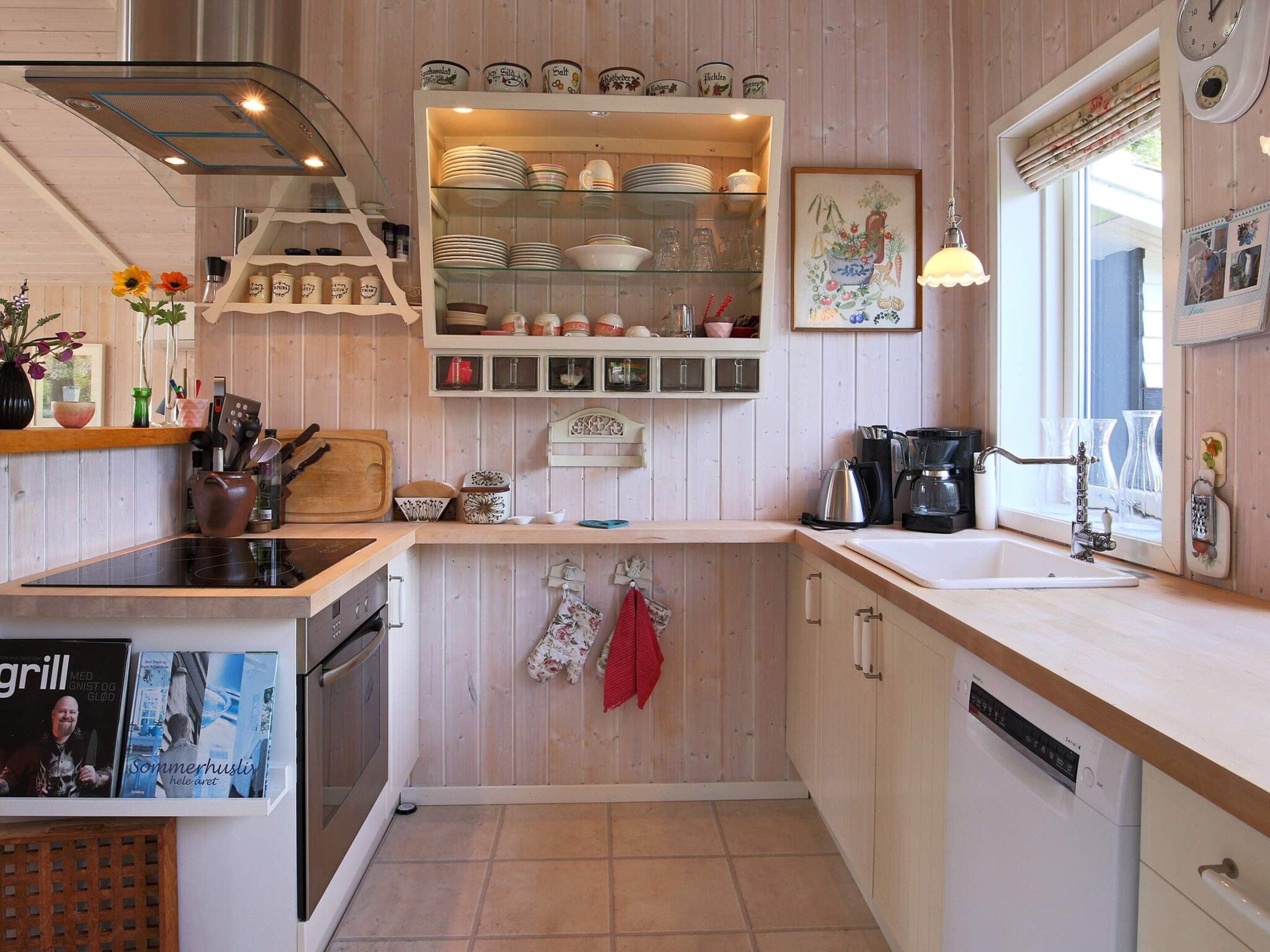 Une cuisine équipée d’un lave-vaisselle, d’une cuisinière et d’un évier. On y trouve une étagère avec de la vaisselle et une horloge au mur.