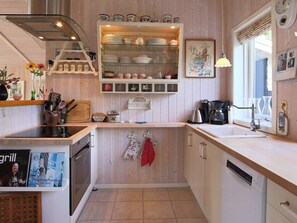 A kitchen with a built-in dishwasher, a stove, and a sink. There is a shelf with dishes and a clock on the wall. - 4 Person Holiday Home in Follenslev (Follenslev)
