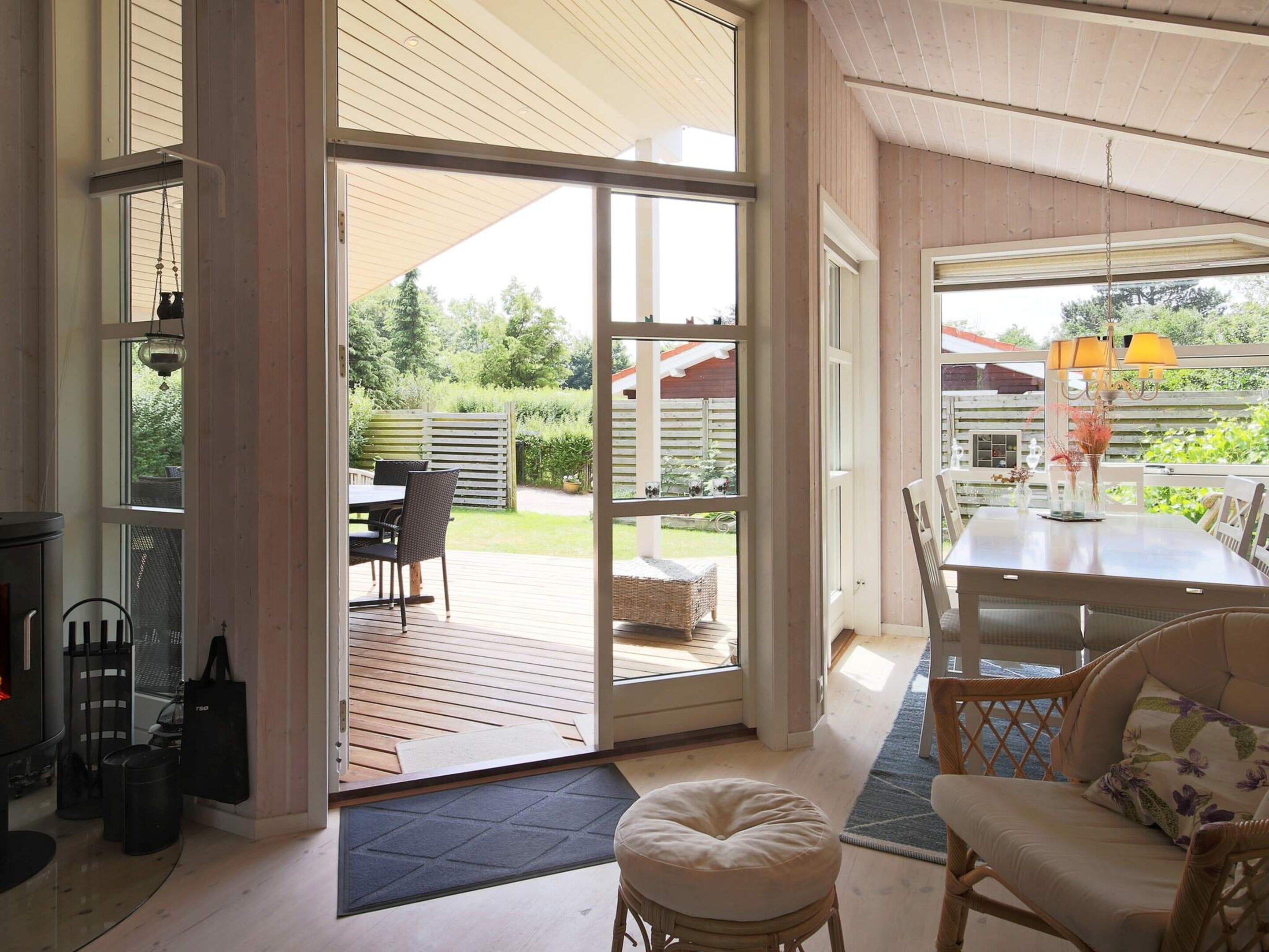 An open-plan living area with a sliding glass door leading to a patio, a dining table with chairs, and a seating area with cushions.