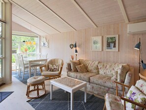 A cozy living room with a wooden ceiling, a floral sofa, a white coffee table, and a dining area with a white table and chairs. - 4 Person Holiday Home in Follenslev (Follenslev)