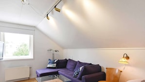 A modern, compact room with a glass-top coffee table, a purple sofa, a wooden side table, and a bed with a quilt. - 6 Person Holiday Home in Kode (Kode)