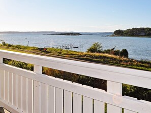 A waterfront property with a white deck overlooking a calm lake, a dock with boats, and a distant island. - 6 Person Holiday Home in Kode (Kode)