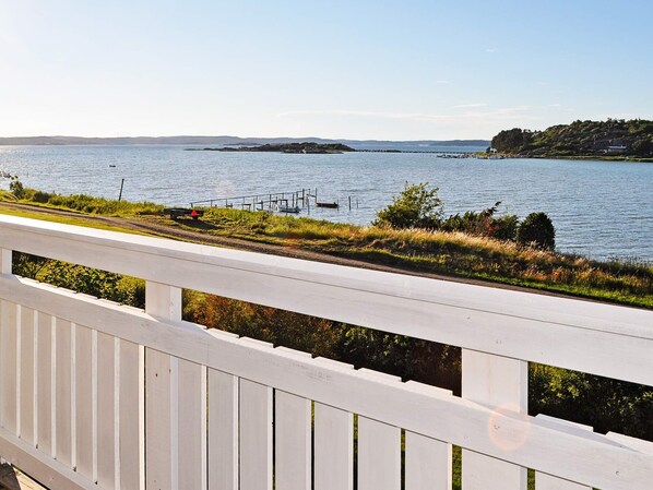 A waterfront property with a white deck overlooking a calm lake, a dock with boats, and a distant island. - 6 Person Holiday Home in Kode (Kode)