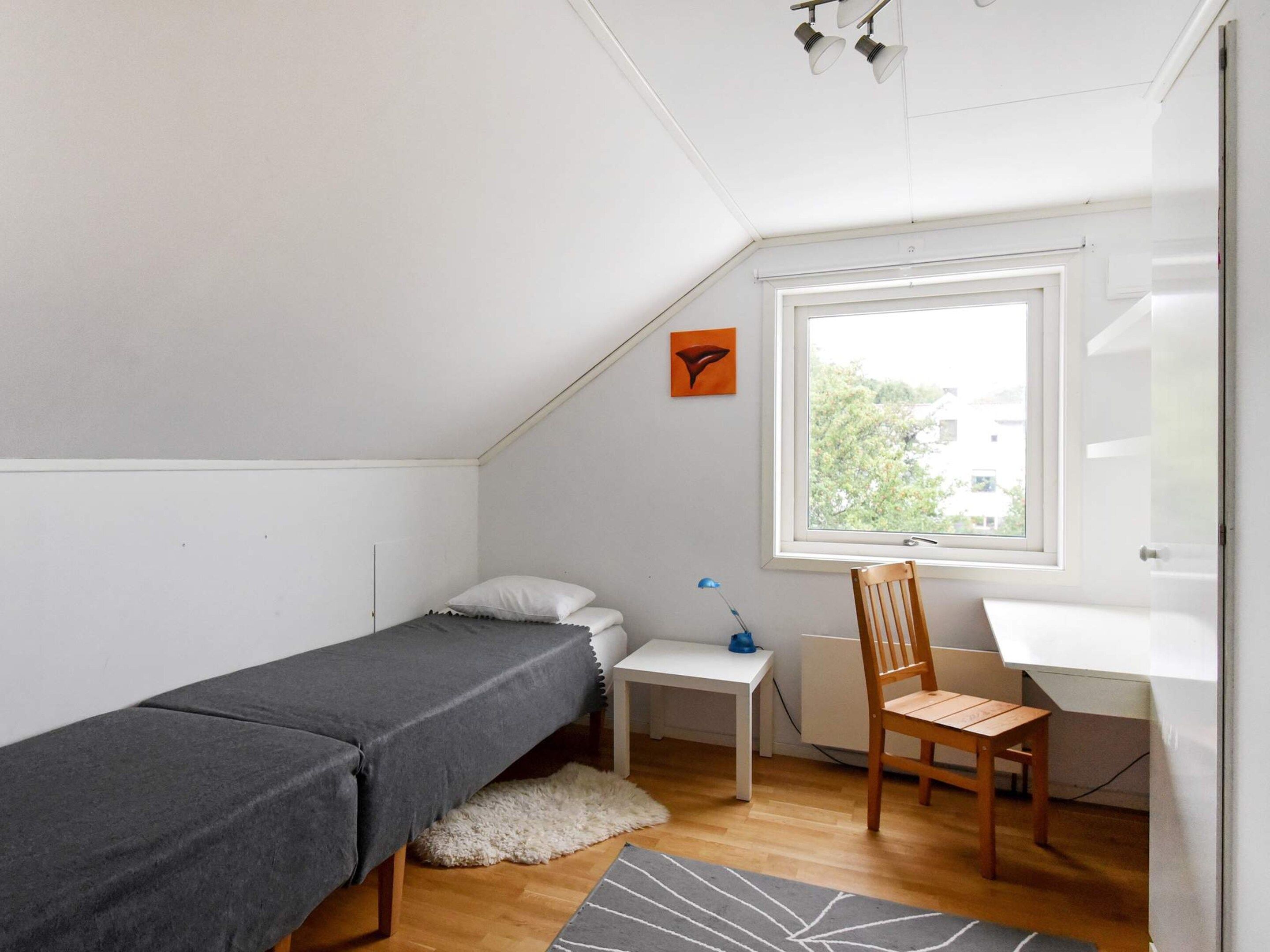 A small, tidy room with a bed, a desk, a chair, and a window.