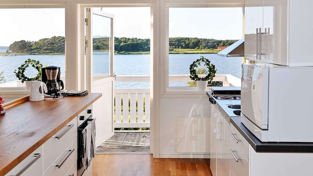 A modern kitchen with a view of a lake, wooden flooring, and white cabinetry. - 6 Person Holiday Home in Kode (Kode)