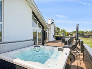 Ein Whirlpool auf einer Holzterrasse mit Blick auf ein Haus und einen Garten.