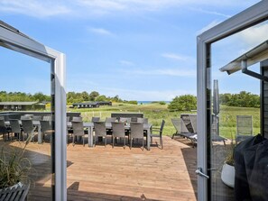 Une terrasse extérieure avec des tables et des chaises, une vue sur un champ verdoyant et un bâtiment visible au loin.