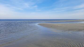Ein Strand mit sanften Wellen, blauem Himmel und einer entfernten Küste.