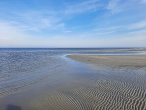 Une plage aux vagues douces, un ciel dégagé et une côte lointaine.