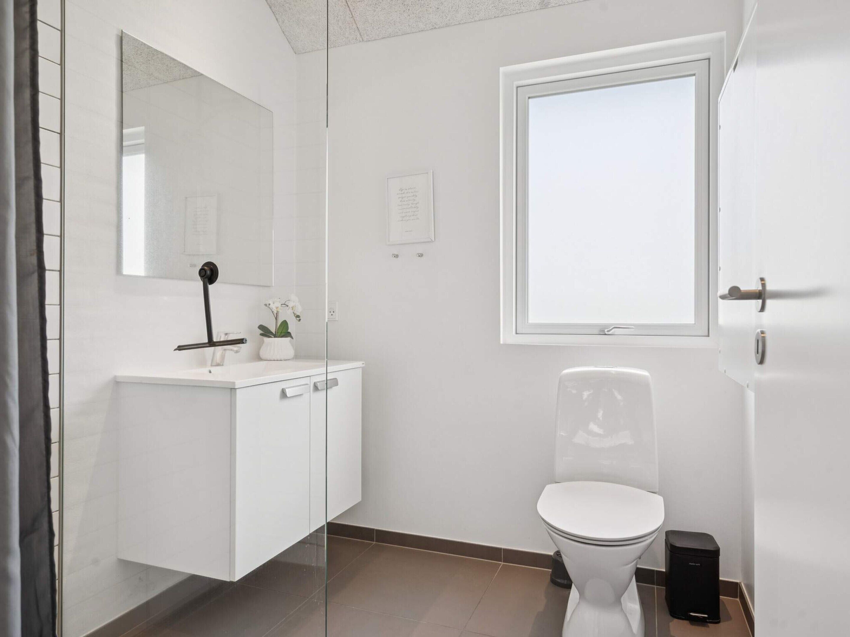 A modern bathroom with a white vanity, a toilet, a window, and a mirror.
