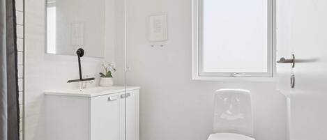 A modern bathroom with a white vanity, a toilet, a window, and a mirror.