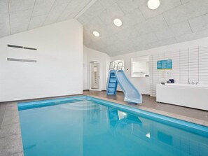Ein Hallenbad mit blauer Rutsche, einer Rezeption und einer gefliesten Wand mit Rastermuster.