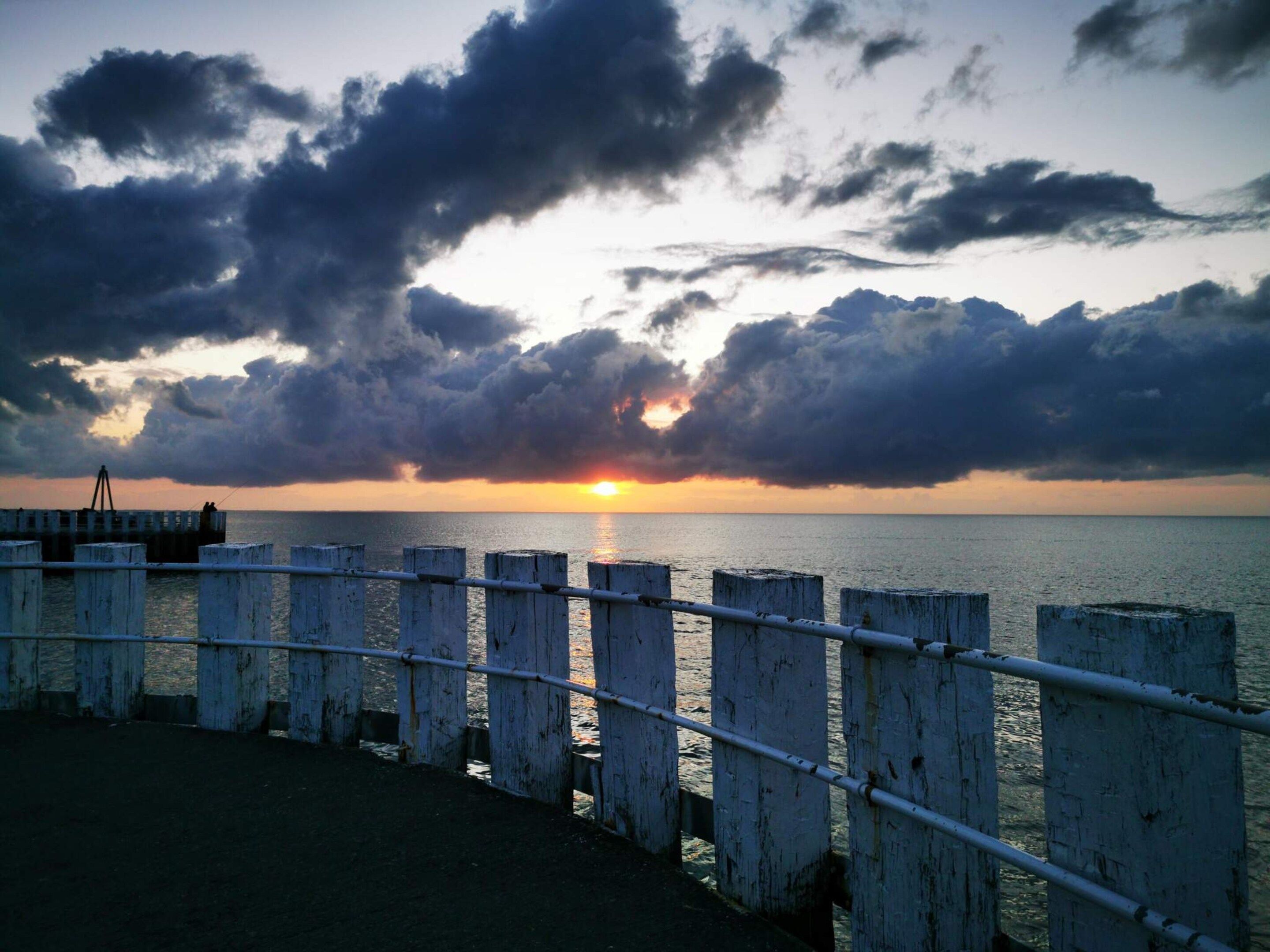 A coastal scene with a sunset, a pier, and a railing.
