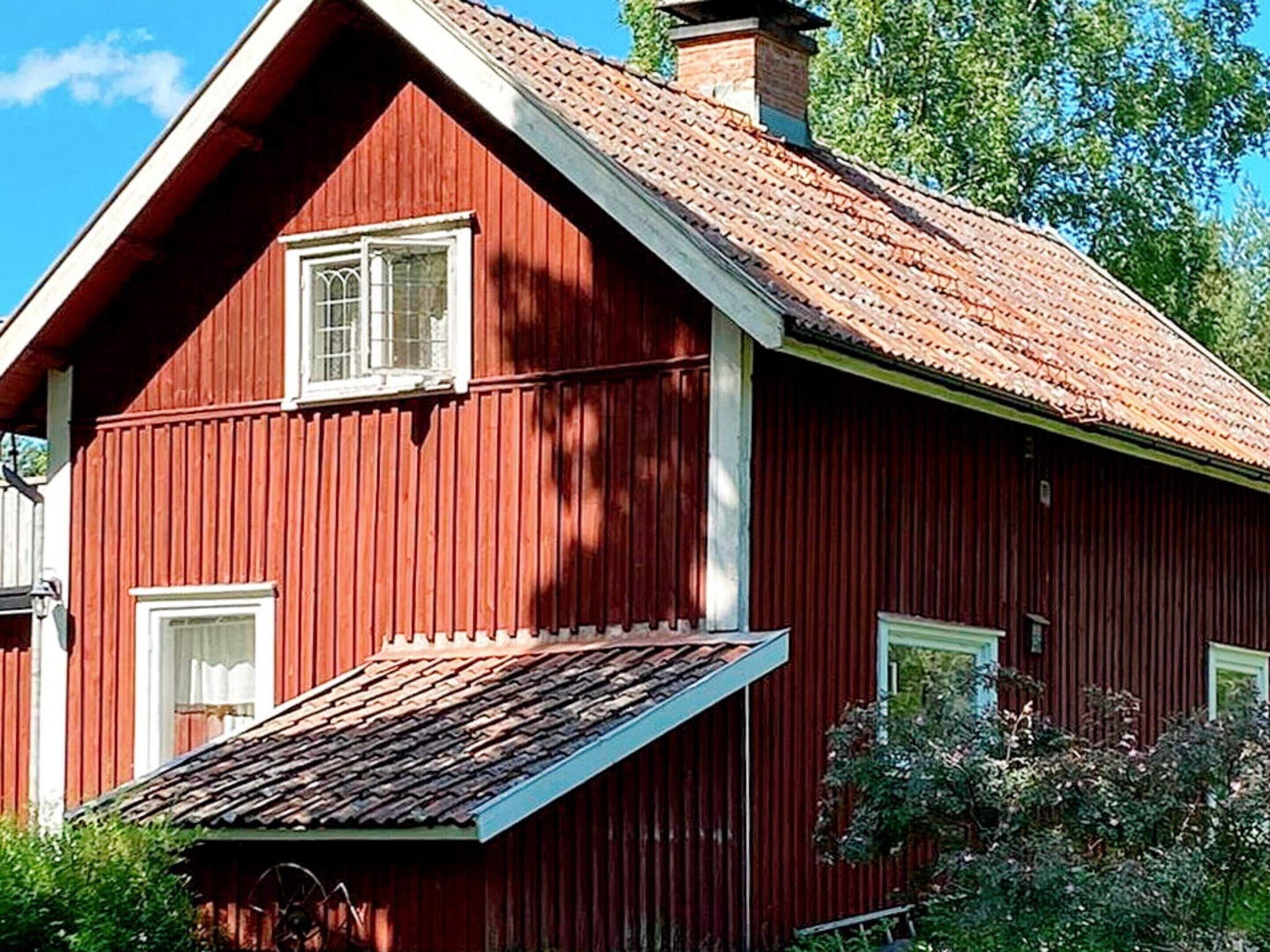 A red wooden house with a sloped roof and two windows.