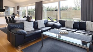 A modern living room with a sectional sofa, a glass coffee table, and a dining area with a table and chairs. - 5 Star Holiday Home in Hadsund (Hadsund)