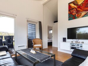 A modern living room with a glass coffee table, leather sofa, and a flat-screen TV.