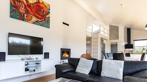 A modern living room with a black leather sofa, a glass coffee table, a fireplace, a flat-screen TV, and a painting on the wall. - 5 Star Holiday Home in Hadsund (Hadsund)