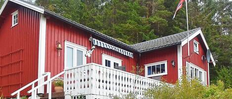 A red wooden house with a white balcony, a flag, and a bell.