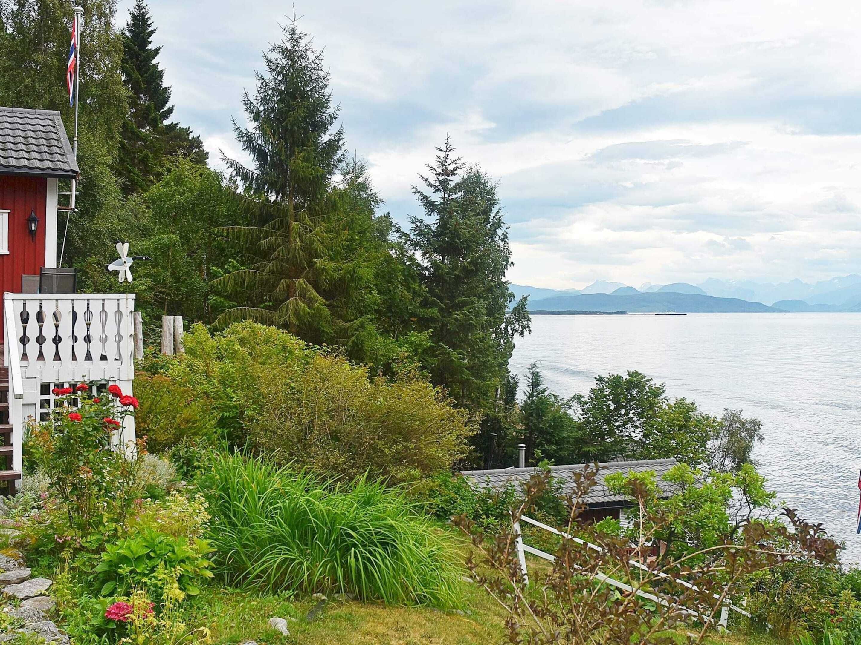 Una proprietà sul lago con un edificio rosso, una recinzione bianca e vegetazione rigogliosa.