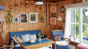 A cozy room with wooden walls, a blue sofa, a wooden table, and a red trunk.