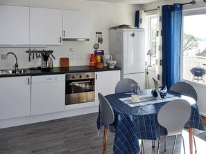 A compact kitchen with white cabinets, a stainless steel oven, and a dining table with a blue tablecloth. - 4 Star Holiday Home in Onarheim (Tysnes)