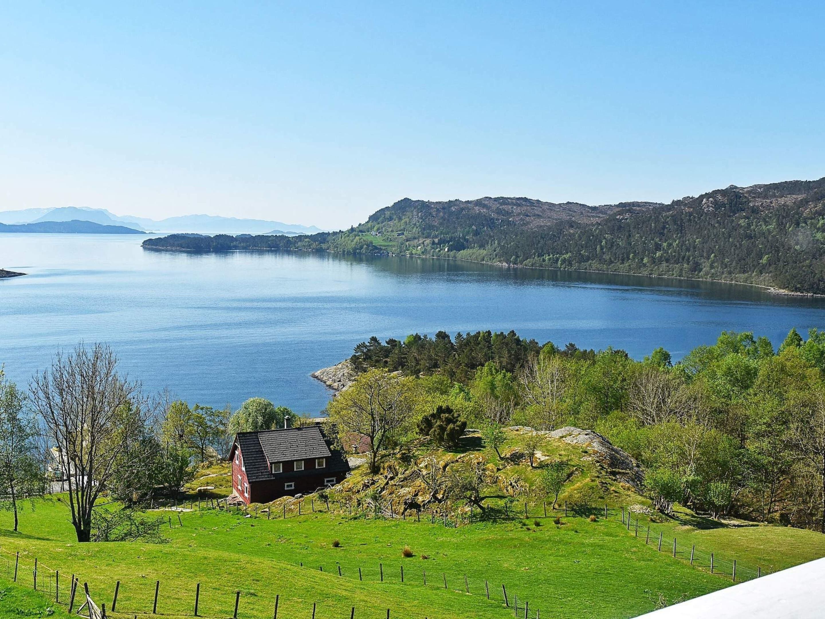 A rural landscape with a lake, a house, and surrounding greenery.