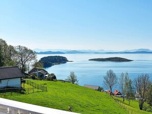 Eine Küstenlandschaft mit einem grasbewachsen Hügel, einem kleinen Haus und einem Gewässer.