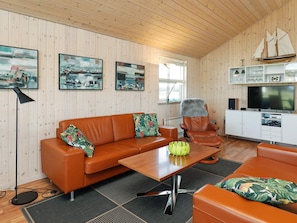 A room with a wooden ceiling, a brown leather sofa, a wooden coffee table, a television, and a ship model on the wall. - 5 Star Holiday Home in Hirtshals (Hirtshals)