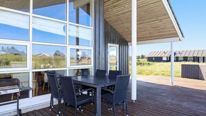 Un espacio de comedor al aire libre techado, con una mesa y sillas, ventanas amplias y vistas del paisaje circundante.