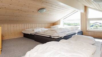 A bedroom with a sloped ceiling, wooden paneling, a large window, and a bed with white bedding.