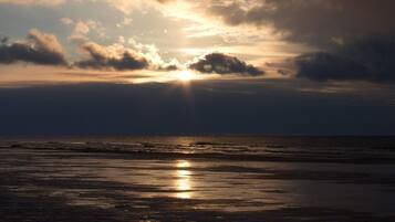 A beach with the sun reflecting on the wet sand.