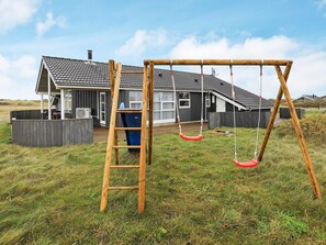 A wooden swing set in front of a house with a sloped roof and a fenced yard.