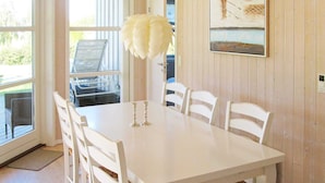 A dining area with a white table and chairs, a white feathered decoration, and a painting on the wall. - 5 Star Holiday Home in Rude (Bisserup)