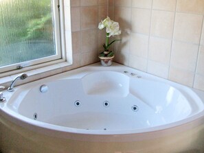 Een badkamer met een bad, een raam en een potplant.