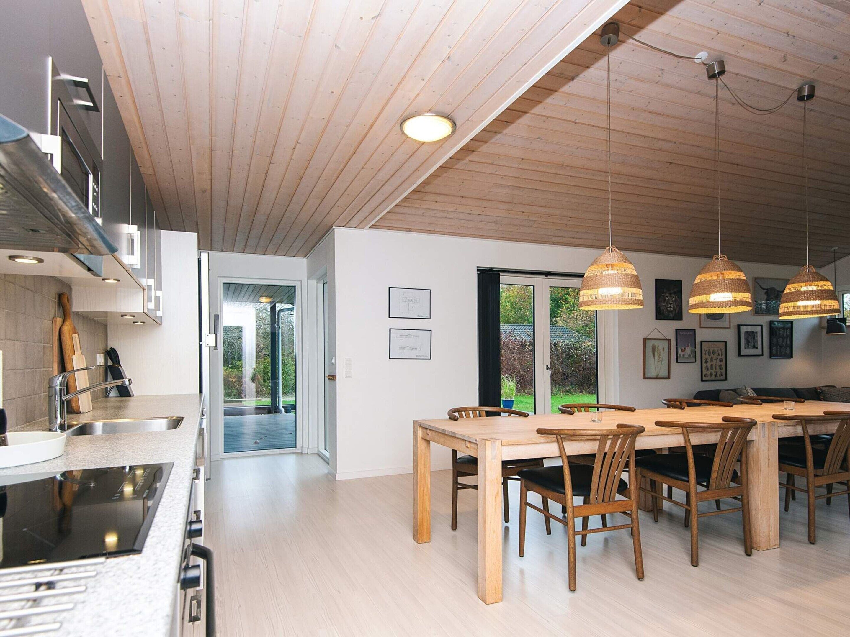 A modern kitchen with a large island, wooden ceiling, and pendant lights.