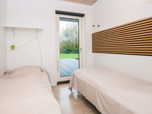 A bedroom with two beds, a wooden slatted headboard, a small green light, and a door leading to an outdoor deck.