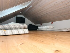 A loft bedroom with a sloped ceiling, a television mounted on the wall, and a bed with striped bedding. - 4 Star Holiday Home in Glesborg (Glesborg)