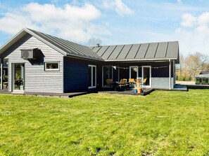 A modern house with a covered patio area, large windows, and a grassy yard. - 4 Star Holiday Home in Glesborg (Glesborg)