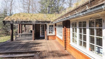 Una terraza de madera con una pérgola, un espacio de estar cubierto y un edificio con grandes ventanales.
