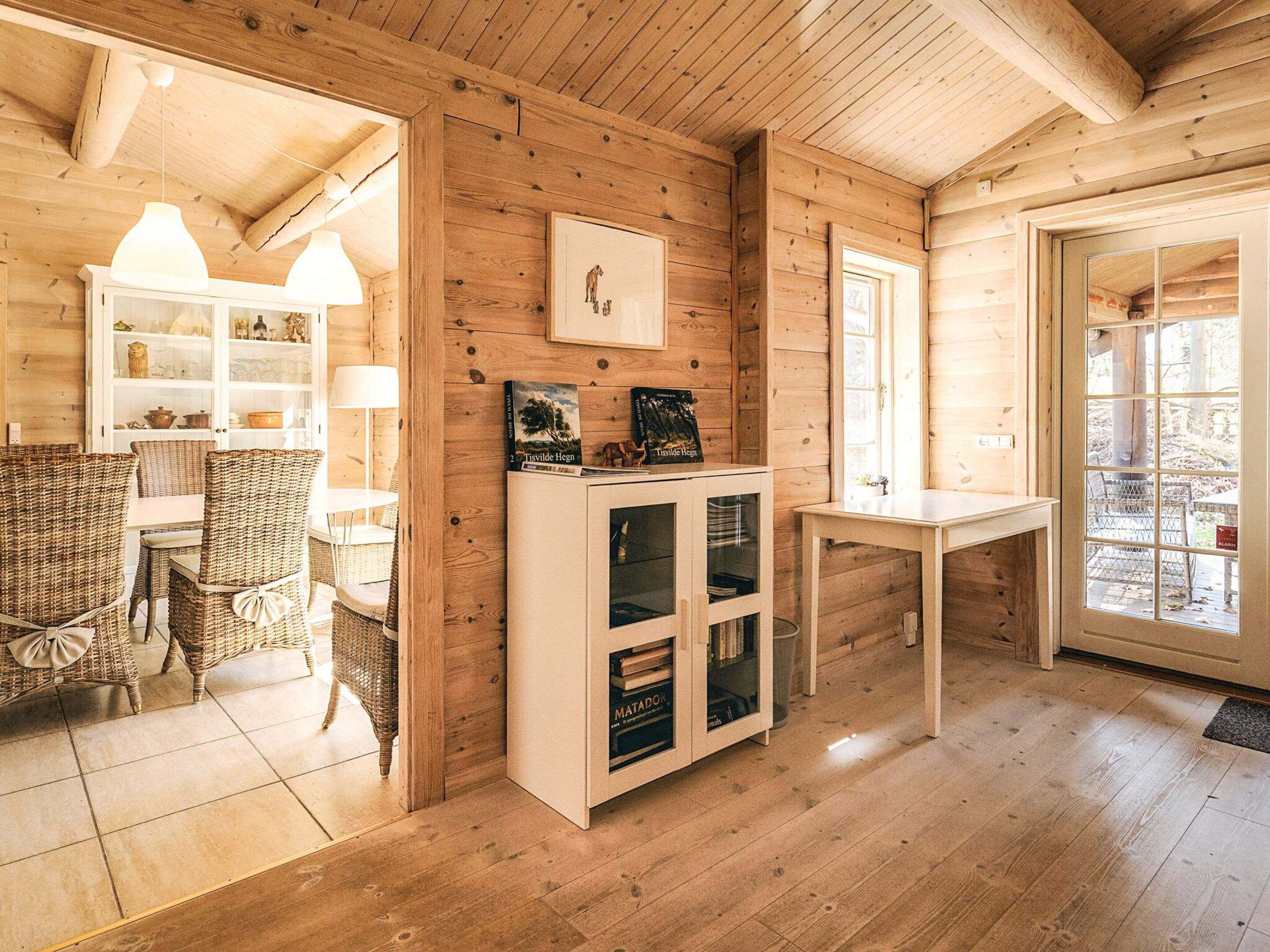 Un interior de madera con zona de comedor, un aparador con puertas de cristal y una ventana.