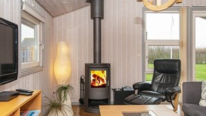 A cozy living room with a wood-burning stove, leather chairs, a TV, and a bookshelf. - Tranquil Retreat With Spa - By Traum Ferienwohnungen (Hemmet)