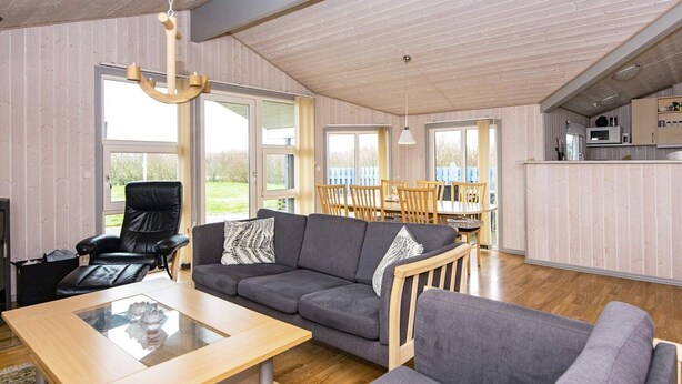 A spacious living room with a grey sofa, a black leather chair, and a wooden coffee table. There is a dining area with wooden chairs and a table, and a kitchen area with a microwave and cabinets. - Tranquil Retreat With Spa - By Traum Ferienwohnungen (Hemmet)
