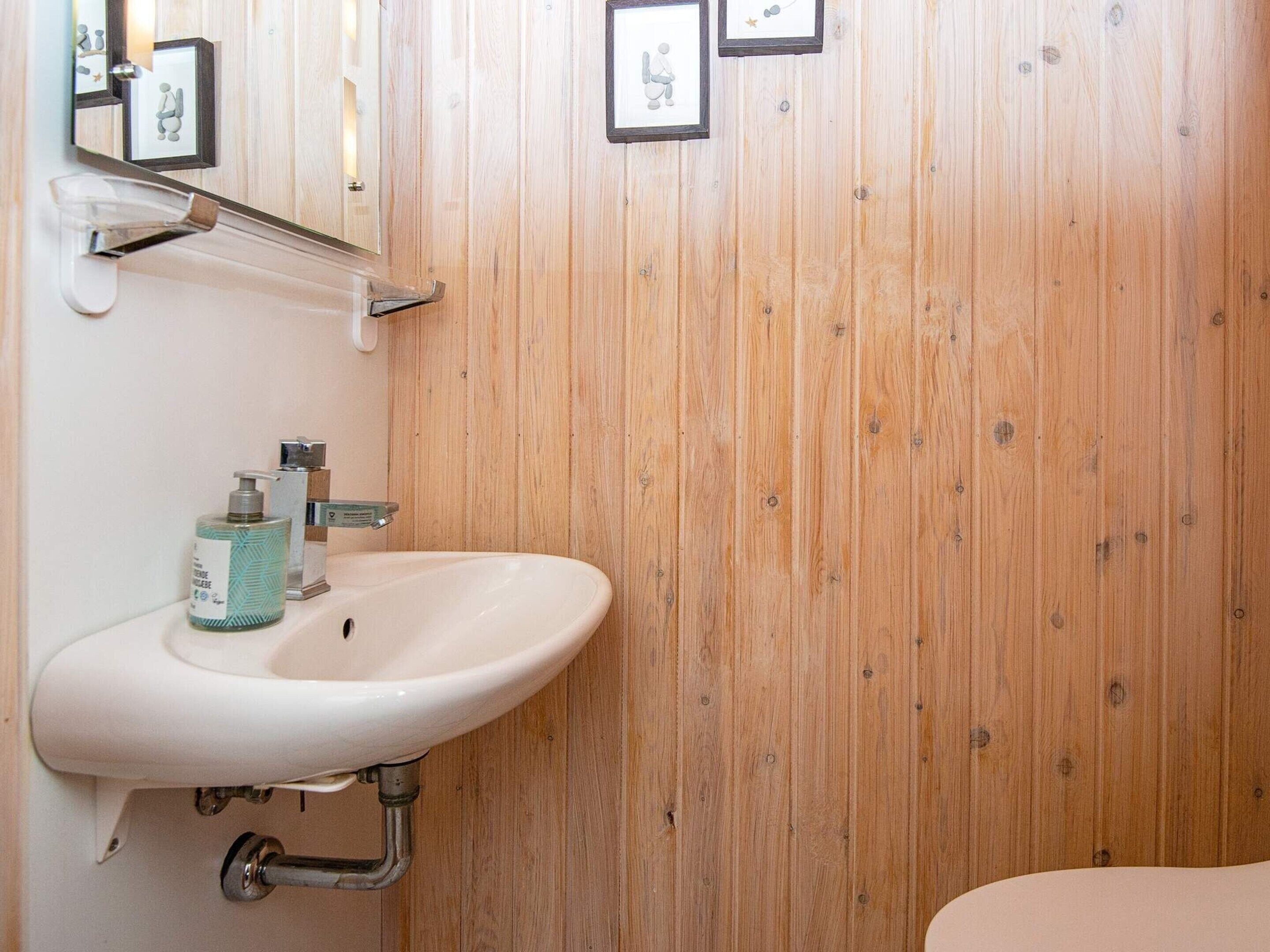 A bathroom with a wooden wall, a white sink, and a mirror.