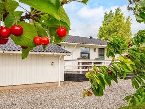 A white building with a gravel driveway and a tree with red fruits in the foreground.