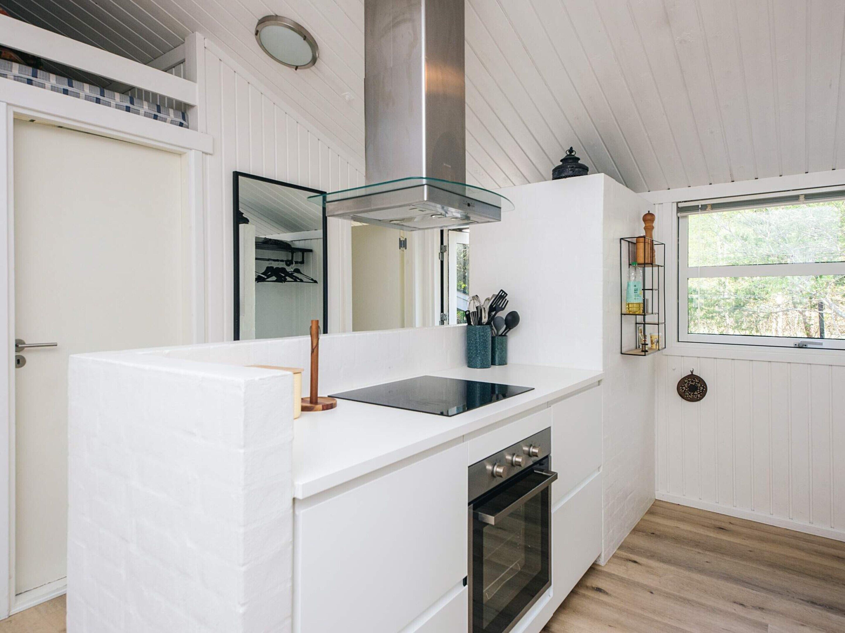 Een moderne keuken met een wit aanrecht, een glazen afzuigkap, een ingebouwde oven en een raam met uitzicht op bomen.