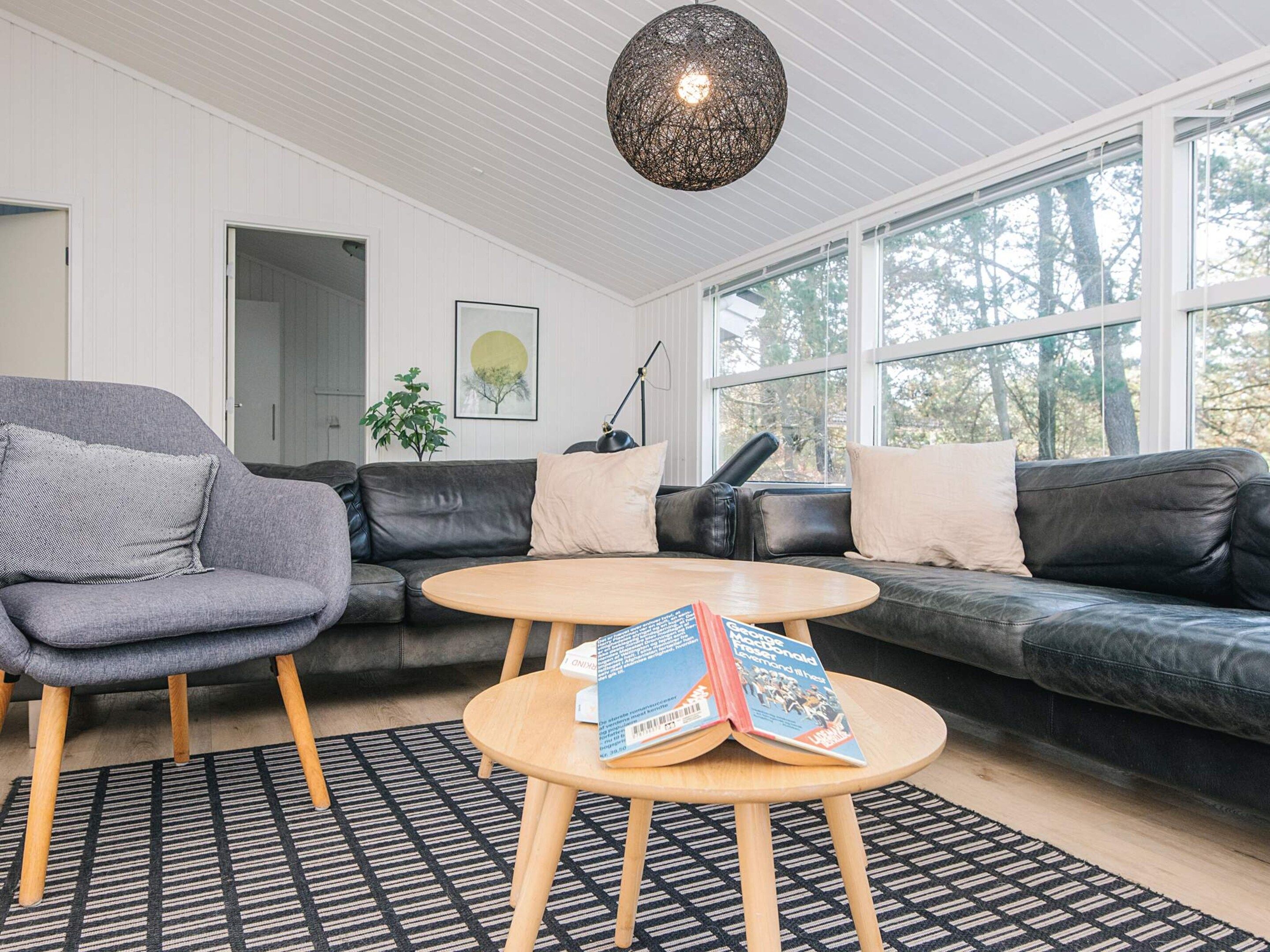 Uma sala de estar moderna com um sofá cinza, um sofá de couro preto, uma mesa de centro de madeira e um tapete estampado.